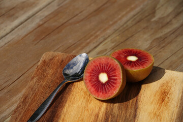 A delicious red kiwifruit sliced in half, with a teaspoon on a wooden surface