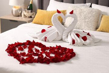 Honeymoon. Swans made with towels and beautiful heart of rose petals on bed