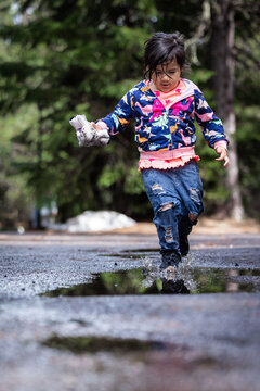 A young girl is playing in the rain, splashing in puddles