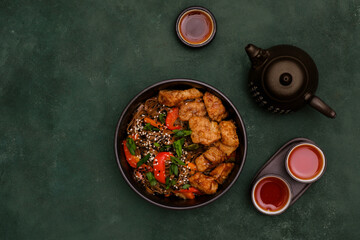 Fried Udon with Chicken and vegetables, chinese teapot and cups of tea on dark green background. Top view. Asian food.