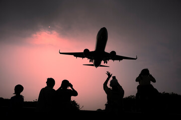 Silhouette of a group of people watching the plane at sunset