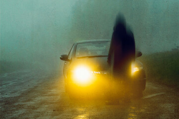 A horror concept of a blurred  spooky figure. In front of a car. On a dirt track on a creepy foggy...