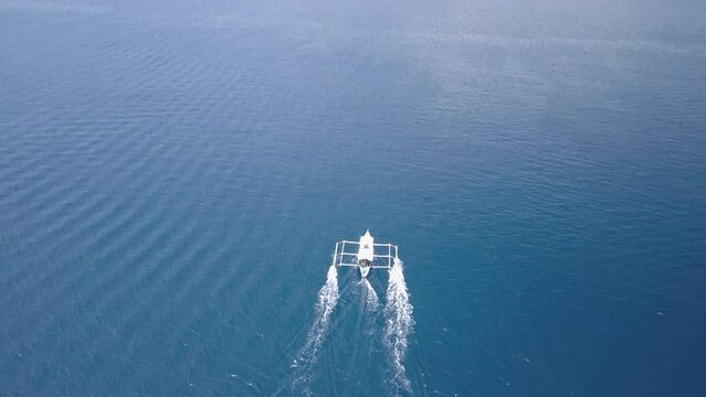 Aerial Tilt Up Shot Of Outrigger Moving In Blue Wavy Sea Towards Rock Formations On Sunny Day - Palawan, Philippines