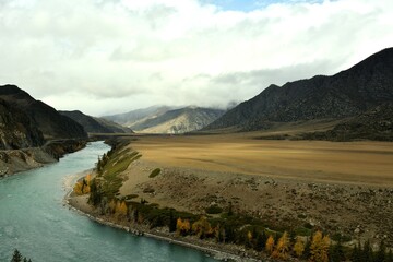 A turn in the course of a wide turquoise river flowing through a huge valley in the mountains on a...
