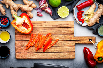 Food and cooking background. Gray table with chopped paprika. Zucchini, raw vegetables, spices and ingredients for cooking vegan Asian dishes with ginger, garlic, soy sauce, top view
