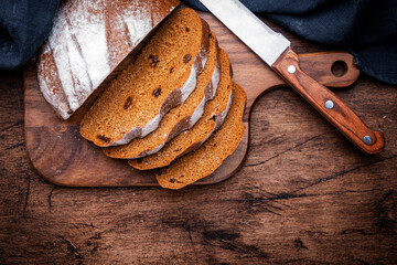 Sourdough rye bread pieces on wooden board, bread knife and black kitchen towel. Rustic table background, top view