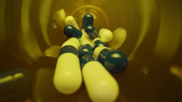 Spilled Pill Bottle, Pull Out. Macro wide angle extreme close up (ECU) pulling out of a bottle over some scattered blue and white pill capsules.