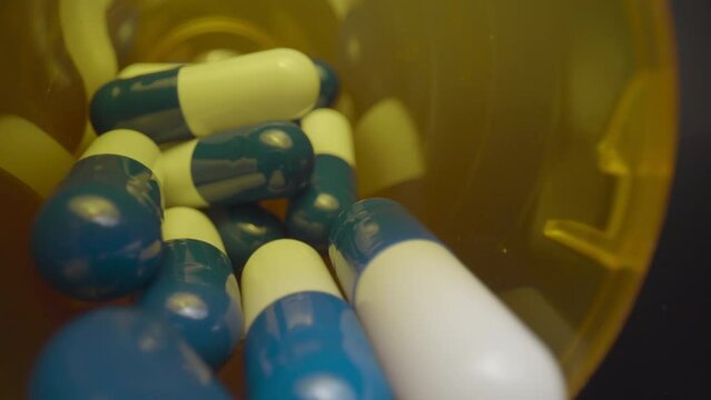 Spilled Pill Bottle, Reveal. Macro wide angle extreme close up (ECU) pulling out of a bottle and revealing scattered blue and white pill capsules.