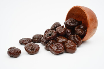 Dried prunes spilling out of a wooden bowl isolated background