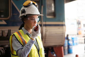 Portrait of railway technician worker in safety vest and helmet working and using a walkie talkie at train repair station