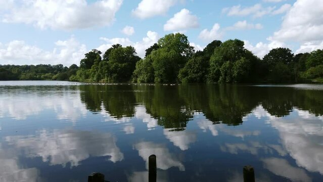 Scenic view of the reflections of clouds, sky, and trees in the waters of Mote Park Lake, located in Maidstone in the county of Kent in United Kingdom.