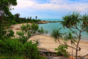 Beach with clear water, fine white sand and large rocks on the edge of the beach with lots of green trees