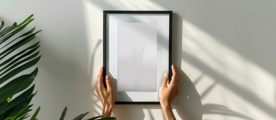 Woman's hands holding a picture frame with an empty space for a poster, displayed vertically on a wall. The room is decorated with the frame as a part of the overall home decor. - obrazy, fototapety, plakaty