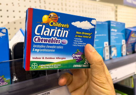 Shopper hand holding a box of Bayer Children's Claritin brand loratadine grape flavored chewable tablets at a local pharmacy shelf