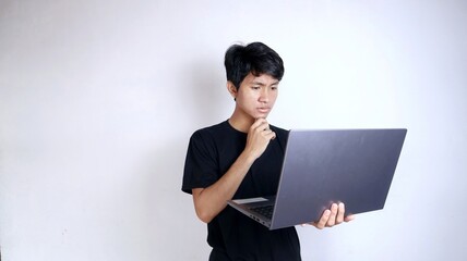 young asian man excited with gesture holding laptop thinking surprised confused