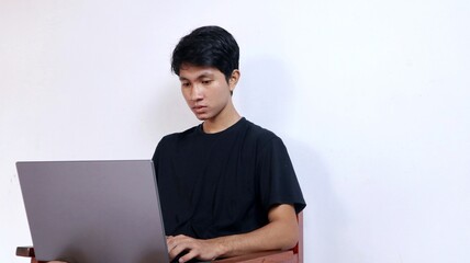 young asian man with gesture sitting on a chair using a laptop