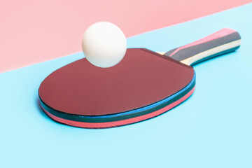 Racket with table tennis ball on blue and pink background close-up.