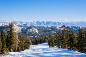 An empty, snowy ski slope with a view of snow-capped mountains in the distance. Mammoth Lakes, California