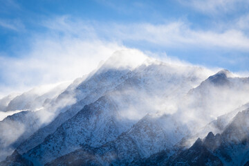 A closeup view of a mountain peak covered in snow as the wind swirls clouds around it. Aspen...