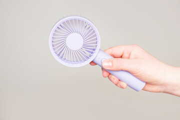 Female hand holding a small fan on gray background close-up.