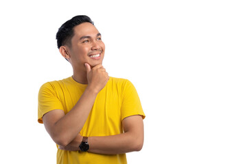 Happy Asian young man looking aside at empty space, touching chin, thinking of new good...