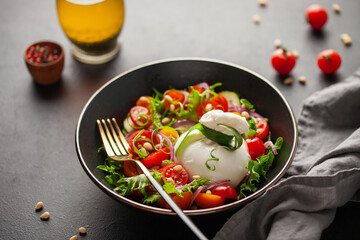 Salad with traditional italian burrata cheese. Burrata ball with cherry tomatoes, cucumber slices, onion  and pine nut in bowl on the table