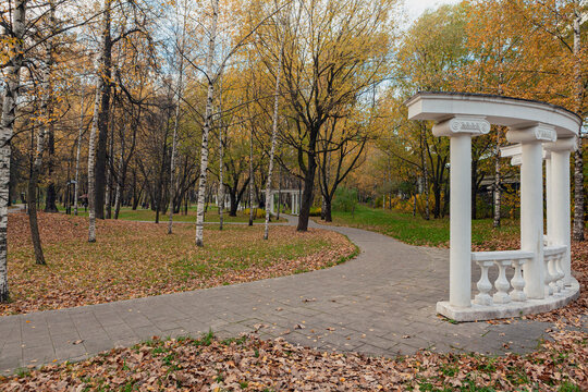 A path in an autumn park with a white gazebo in the background.