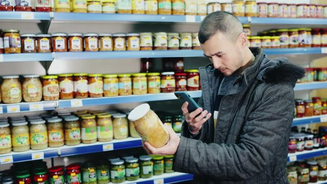 Man scans barcode on jar of sauerkraut using a smartphone while shopping in a grocery store. High quality 4k footage