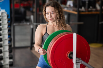 Fototapeta na wymiar Caucasian forty year old woman putting a weight plate on a barbell in the gym. 