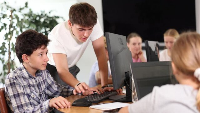 Young guy teacher teaches boy student to work with computer at lesson in classroom