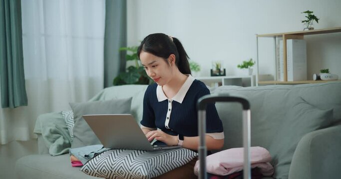 Footage dolly shot, Asian teenager woman sitting on sofa using laptop for prepare booking hotel and airplane ticket for travel. backpacker travel concept.