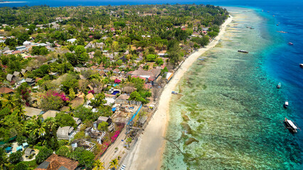 Aerial view of a sandy tropical beach and small resorts next to a warm ocean and coral reef (Gili...