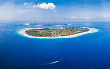 Aerial view of a small boat passing a tropical island in a blue ocean (Gili Meno)