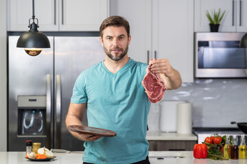 Handsome man cooking meat beef steak in kitchen. Portrait of casual man cooking with meat...