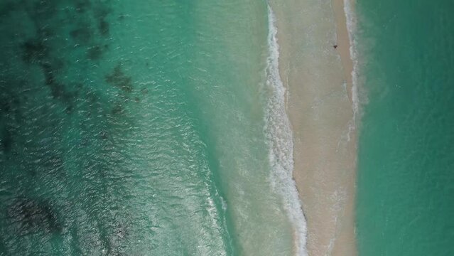 The clear turquoise sea gently meeting the sandy beach at cayo de agua, aerial view