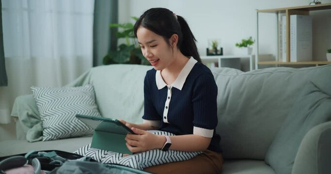 Footage slow motion shot, Asian teenager woman sitting on sofa planning vacation trip and searching information on digital tablet, travel and lifestyle.