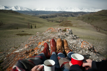 Close-up of hands with mugs and feet against background of mountains. First-person view - 766807965