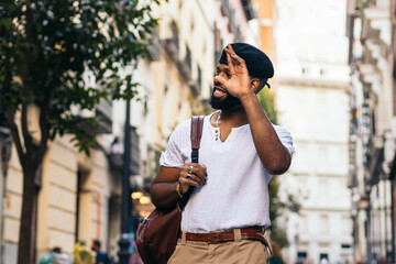 Stylish black man walking on the city street waving someone