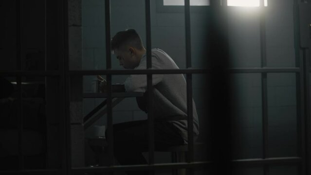 Caucasian young prisoner eats prison food sitting at the table in prison cell. Teenage criminal, inmate serves imprisonment term for crime in jail. Juvenile detention center or correctional facility.
