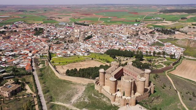 View from drone of Castillo de Belmonte, ancient walled fortified castle on background of townscape and extensive agricultural fields on sunny spring day, Spain