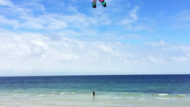 A man stands in the water on the beach and tries out the colorful kite in the wind. The tropical beach in Siquijor Island in the Philippines. The clouds in the blue sky and the turquoise water.