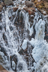 Chilly cascade waterfall, where water rushes over icy rocks, intertwining liquid flow with frozen...