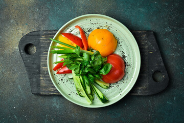 Cutting fresh vegetables: tomatoes, paprika, parsley, cilantro, onions. On a plate. On a dark stone background.