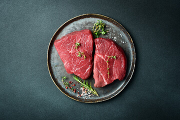 Juicy raw piece of selected veal on a plate with spices and herbs, on a stone background. Veal, steak. Top view.