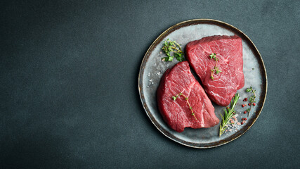 Juicy raw piece of selected veal on a plate with spices and herbs, on a stone background. Veal, steak. Top view.