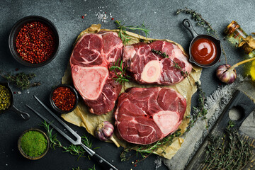 Raw ossobuco steak with rosemary and spices on a black stone background. Free space for text.