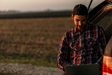 Man working remotely from his vehicle's trunk, illuminated by the warm glow of the setting sun