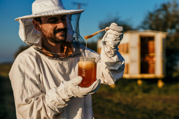 Dedicated beekeeper in protective gear inspecting honey frames outdoors