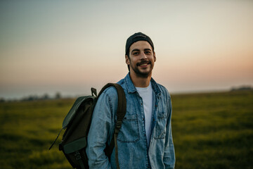Hipster guy hiking in scenic countryside under the setting sun