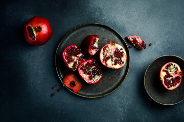 Sliced pieces of fresh pomegranate on a black stone plate. On a dark gray concrete background.